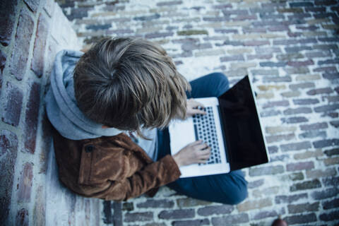 Teenager mit Laptop und auf einem Steinboden in der Stadt sitzend, lizenzfreies Stockfoto