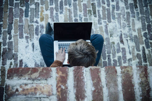 Teenager mit Laptop und auf einem Steinboden in der Stadt sitzend - ANHF00194
