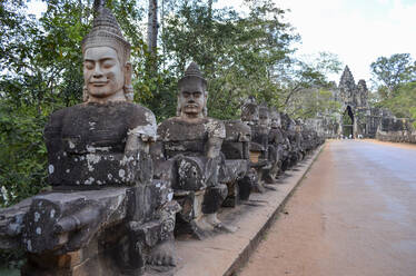 Ankor Wat, ein historischer Khmer-Tempel aus dem 12. Jahrhundert und UNESCO-Weltkulturerbe. Büsten und Statuen von Gottheiten und Wächterfiguren entlang eines Weges zu einer Stupa und einem Eingangsbogen. - MINF13407