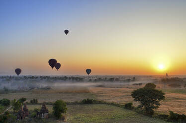 Heißluftballons über der Landschaft mit fernen Tempeln bei Sonnenuntergang, Bagan, Myanmar. - MINF13418