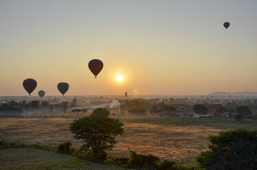 Heißluftballons über der Landschaft mit fernen Tempeln bei Sonnenuntergang, Bagan, Myanmar. - MINF13419