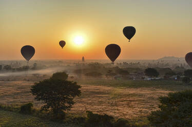 Heißluftballons über der Landschaft mit fernen Tempeln bei Sonnenuntergang, Bagan, Myanmar. - MINF13420