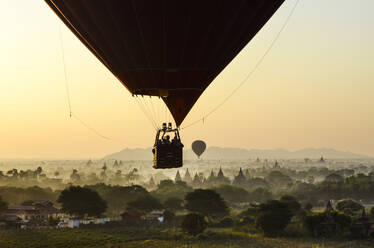 Heißluftballon über Landschaft mit Tempeln bei Sonnenuntergang, Bagan, Myanmar. - MINF13421