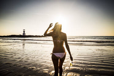 Rear view of woman walking toward the beach during sunset. - MINF13447