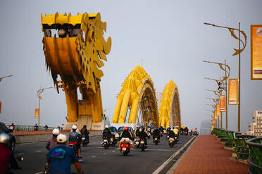 Rückansicht von Pendlern auf Motorrädern, die eine Brücke in Form eines Drachens überqueren. - MINF13468