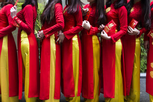 Nahaufnahme einer Reihe junger Frauen in traditioneller roter und gelber Kleidung vor einer Hochzeit. - MINF13481