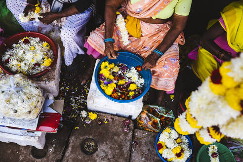 Nahaufnahme von Frauen, die auf einem Markt Blumen an Schnüren befestigen. - MINF13490