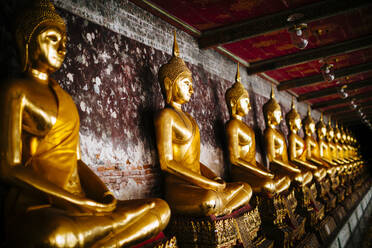 Close up of a row of golden Buddha statues along a wall. - MINF13526