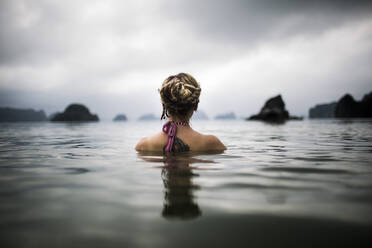 Rückansicht einer Frau mit blondem geflochtenem Haar, die im Meer watet. - MINF13544