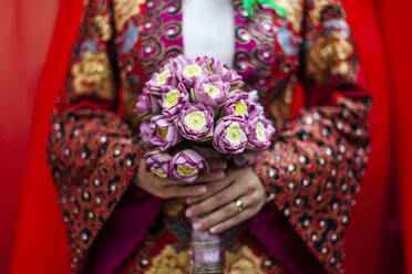 Nahaufnahme einer jungen vietnamesischen Braut in einem farbenfrohen Gewand, die einen Strauß Lotusblumen hält. - MINF13573