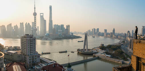 Man admiring view over Huangpu River & Shanghai skyline in early morning, Shanghai, China - MINF13594