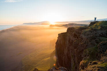 Mann mit Blick auf den Sonnenuntergang von der Halbinsel Dyrholaey, nahe Vik, Südisland (Sudurland), Island, Polarregionen - MINF13597