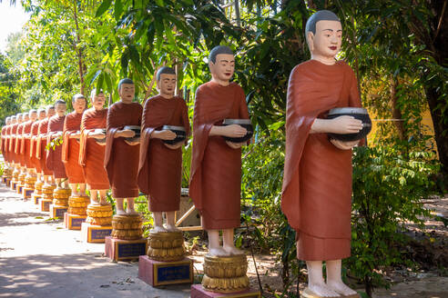 Reihe von buddhistischen Mönchsstatuen mit roten Roben und Almosenschalen in den Gärten des buddhistischen Tempels in Siem Reap - MINF13599