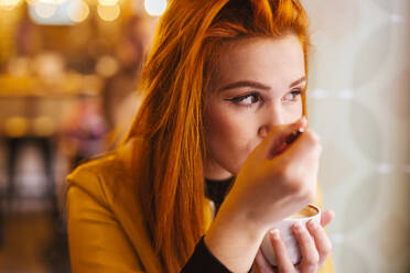 Porträt einer rothaarigen jungen Frau, die einen Cappuccino in einem Café genießt - LJF01278