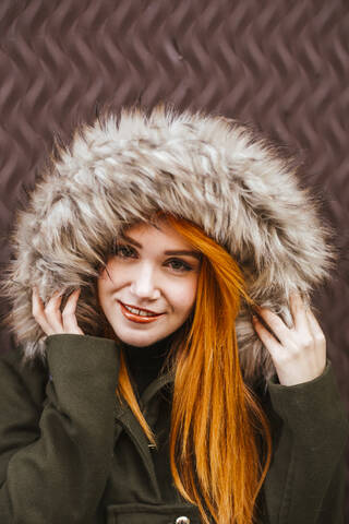 Portrait of smiling redheaded young woman wearing hooded jacket stock photo