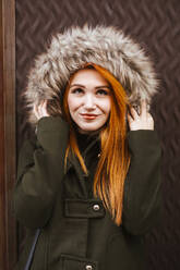 Portrait of smiling redheaded young woman wearing hooded jacket - LJF01293