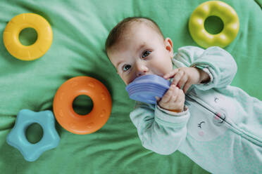 Porträt eines kleinen Mädchens, das auf einer Matte liegt und mit Plastikspielzeug spielt - GEMF03417