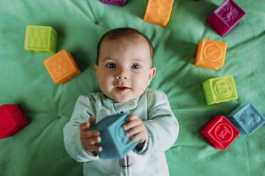 Porträt eines kleinen Mädchens, das auf einer grünen Matte liegt und mit Gummispielzeug spielt - GEMF03420