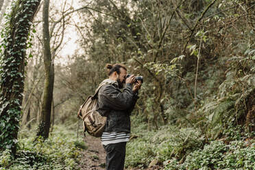 Junger Mann fotografiert im Wald mit seiner Kamera - AFVF05282