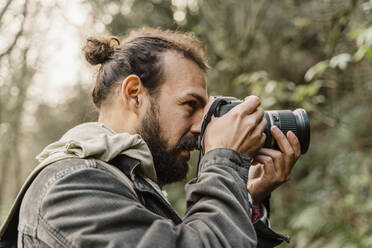 Junger Mann fotografiert im Wald mit seiner Kamera - AFVF05283
