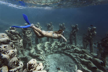 Frau schwimmt in der Nähe einer Unterwasserskulptur von Jason deCaires Taylor, Insel Gili Meno, Bali, Indonesien - KNTF04332
