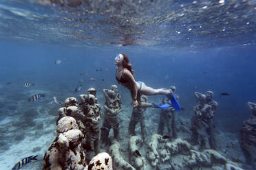 Frau schwimmt in der Nähe einer Unterwasserskulptur von Jason deCaires Taylor, Insel Gili Meno, Bali, Indonesien - KNTF04334