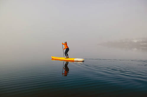 Woman stand up paddle surfing on a lake in the fog - DGOF00298