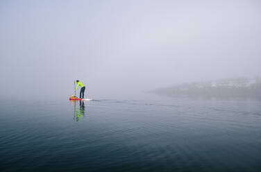 Mann beim Stand Up Paddle Surfing auf einem See im Nebel - DGOF00300