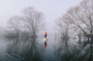 Frau Stand Up Paddle Surfing auf einem See im Nebel - DGOF00305