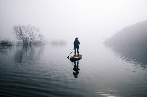 Silhouette einer Frau beim Stand Up Paddle Surfing auf einem See, lizenzfreies Stockfoto