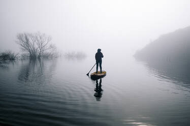 Silhouette einer Frau beim Stand Up Paddle Surfing auf einem See - DGOF00308