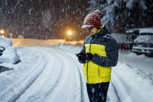 Man using cell phone in snowfall at night - CJMF00245