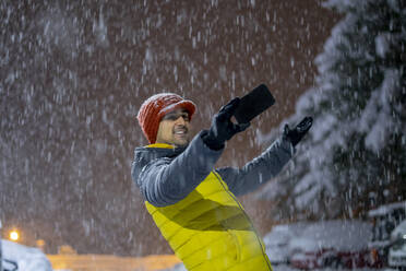 Smiling man taking a selfie in snowfall at night - CJMF00246