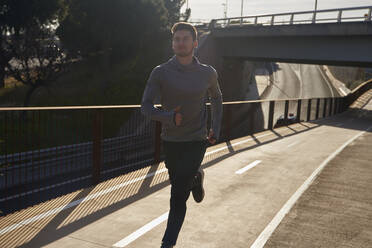 Man running on a road in sunlight - PACF00176