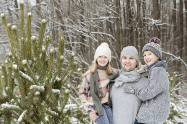 Portrait of happy father with two children at a fir tree in winter - EYAF00927