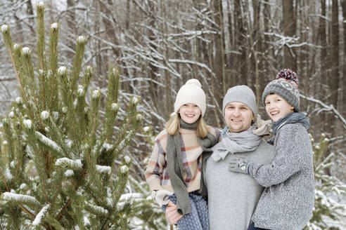 Porträt eines glücklichen Vaters mit zwei Kindern an einem Tannenbaum im Winter - EYAF00927