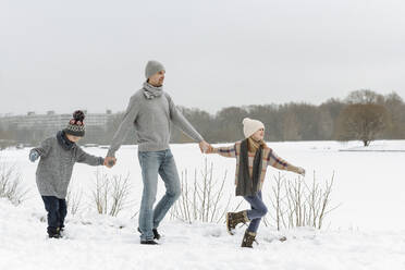 Vater und zwei Kinder gehen in einer Winterlandschaft spazieren - EYAF00929