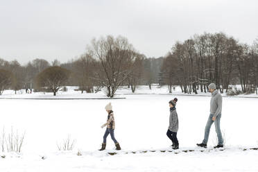 Vater und zwei Kinder gehen in einer Winterlandschaft spazieren - EYAF00930