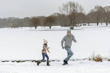 Father and daughter running in winter landscape - EYAF00931