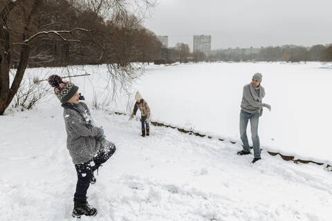 Vater und zwei Kinder liefern sich eine Schneeballschlacht, lizenzfreies Stockfoto