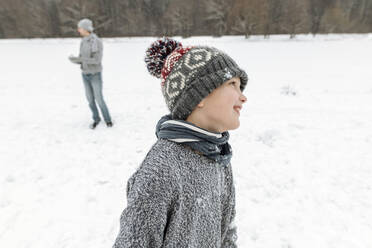 Porträt eines lächelnden Jungen in einer Winterlandschaft mit Vater im Hintergrund - EYAF00934