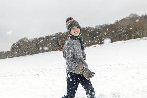 Porträt eines glücklichen Jungen in einer Winterlandschaft mit Schneefall, lizenzfreies Stockfoto