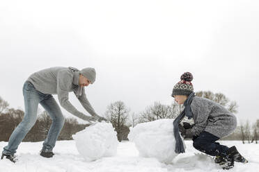 Vater und Sohn bauen Schneemann in Winterlandschaft - EYAF00937