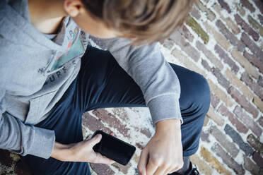 Teenager using smartphone, sitting on stone floor - ANHF00201