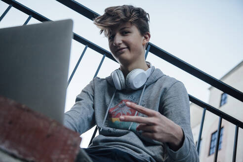 Teenager using laptop in the city, showing victory sign - ANHF00205