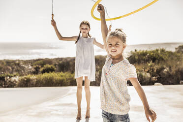 Zwei glückliche Mädchen spielen mit Springseil und Hoola Hoop auf der Terrasse eines Strandhauses - SDAHF00098