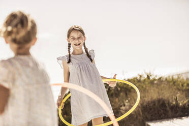 Zwei glückliche Mädchen spielen mit Hoola Hoop auf der Terrasse eines Strandhauses - SDAHF00099