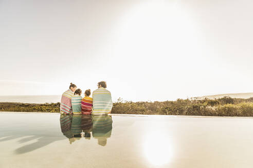 Family wrapped in towels sitting at the poolside at sunset - SDAHF00127