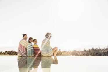 Family wrapped in towels sitting at the poolside at sunset - SDAHF00128