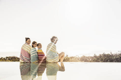 Familie in Handtücher gewickelt am Pool bei Sonnenuntergang - SDAHF00128